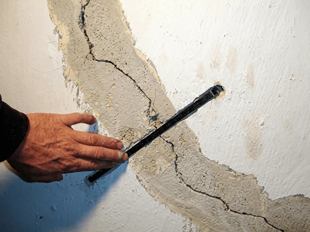 A wall with a large crack is being inspected by a professional in Evansville, IN